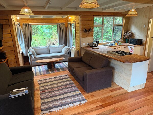 L’intérieur chaleureux d’un chalet comprend un canapé, une petite banquette, une table basse en bois et un coin cuisine avec une cuisinière et un four à micro-ondes.