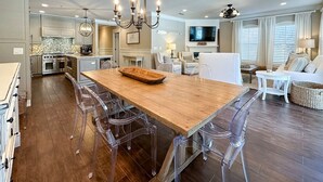 A spacious kitchen with a wooden dining table, clear chairs, and modern appliances.