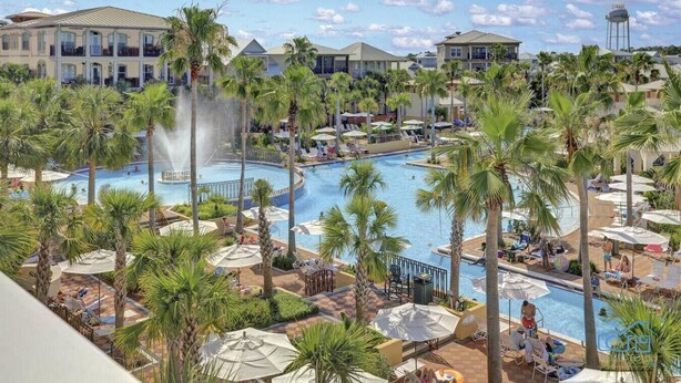 A resort with a large central pool, palm trees, and multiple buildings with balconies.