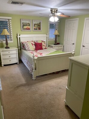 Une chambre à coucher avec un lit, des tables de chevet, un ventilateur de plafond et une porte.