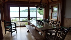 Un espace repas comprenant une grande table et des chaises, un luminaire suspendu et une vue sur un lac, visible à travers de grandes fenêtres.