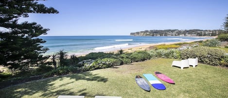 A grassy area with lounge chairs and surfboards, overlooking a beach and ocean.