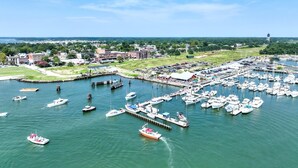 A marina with numerous boats docked, a pier extending into the water, and buildings in the background.