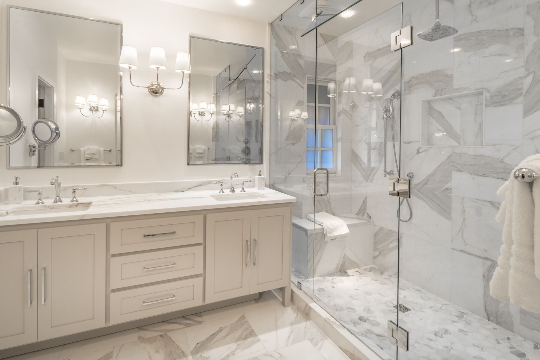 A modern bathroom with a marble shower, a large mirror, and a vanity with two sinks.