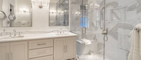 A modern bathroom with a marble shower, a large mirror, and a vanity with two sinks.