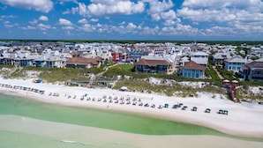 Vista aérea de una zona residencial costera con propiedades frente a la playa, una playa de arena y un cielo despejado.