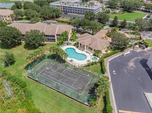 An aerial view of a residential area with a swimming pool, tennis court, and a large building with a flat roof.