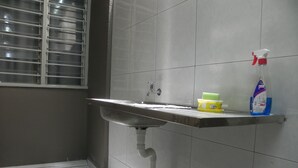 A bathroom with a sink, a window with blinds, and a shelf with cleaning supplies.