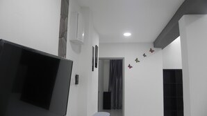 A modern living room with a flat-screen TV, a small stool, and a bottle of cleaning spray.