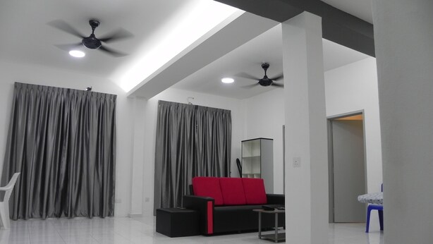 A spacious room with a high ceiling, two ceiling fans, and a modern black sofa with a red cushion.