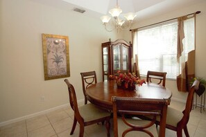 A dining room with a wooden table, chairs, a chandelier, a mirror, and a window with blinds. - Beautiful 4 Bedroom Highlands Reserve Pool Home - 924NHD (Davenport)