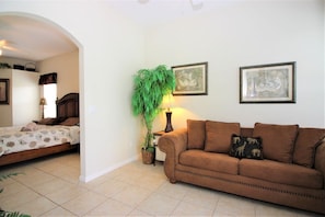 A bedroom with a bed, a brown sofa, a potted plant, and two framed pictures on the wall. - Beautiful 4 Bedroom Highlands Reserve Pool Home - 924NHD (Davenport)