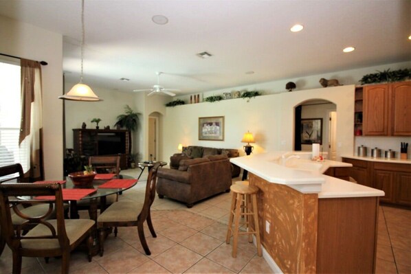 A spacious living area with a dining table, a sofa, and a kitchen with wooden cabinets. - Beautiful 4 Bedroom Highlands Reserve Pool Home - 924NHD (Davenport)