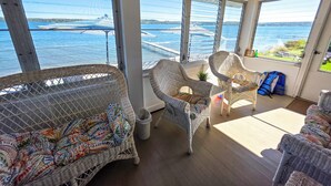 A sunlit room with wicker furniture, large windows offering a view of the water, and a wooden ceiling. - Private Level Beachfront, Fenced Yard, Boat Dock,Kayaks,CentralAir, Great Views! (Auburn)