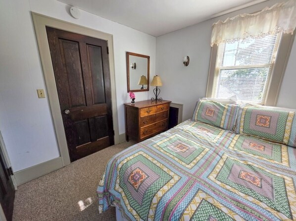 A bedroom with a bed, dresser, and a door.