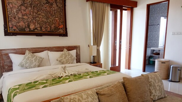 A neatly made bed with a patterned bedspread, a wooden headboard, and multiple pillows. - VIP Green Studio Apartment Seminyak (Kuta, Badung)
