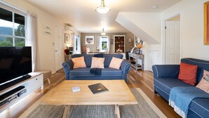 A spacious living room with a large TV, two sofas, a wooden coffee table, and a staircase leading to another level. - BlueMill Cottage Bright - The Complete Luxury Getaway (Bright)