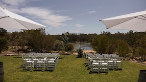 An outdoor wedding venue with rows of white chairs and large white umbrellas, set against a backdrop of trees and a river. - Pet friendly accommodation on the Murray River (Murtho)