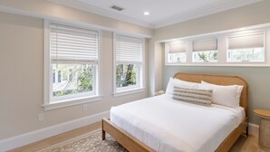 A bedroom with a large bed, three windows with blinds, a small round table, and a ceiling vent. - 2 Bedrooms w/Loft  and  En-Suite Baths, Walk to Harbor (Newport)