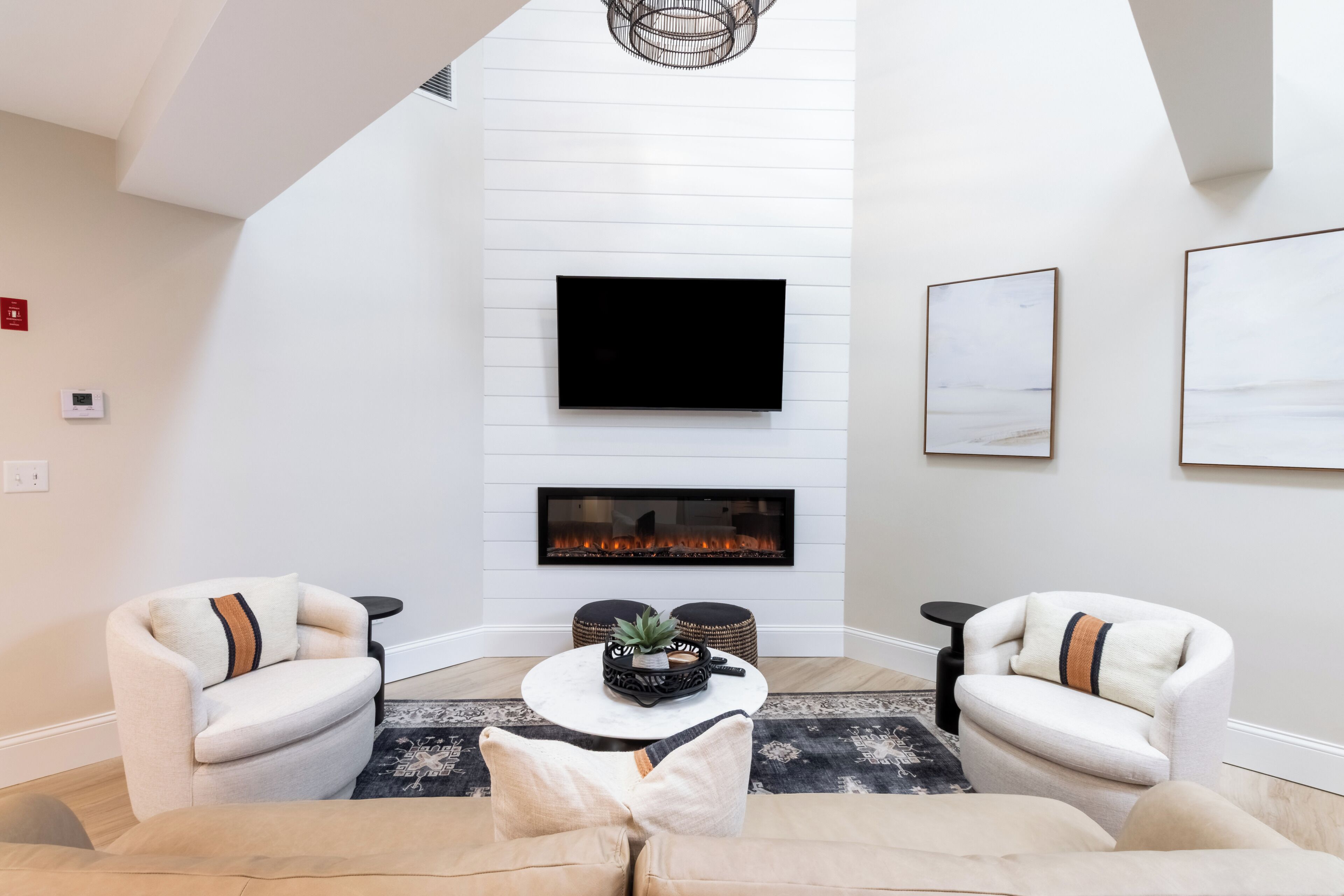 A modern living room with a fireplace, two armchairs, a sofa, and a flat-screen TV mounted on the wall.