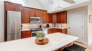 A modern kitchen with wooden cabinets, stainless steel appliances, a marble countertop, and a central island with a plant. - 2 Bedrooms w/Loft  and  En-Suite Baths, Walk to Harbor (Newport)