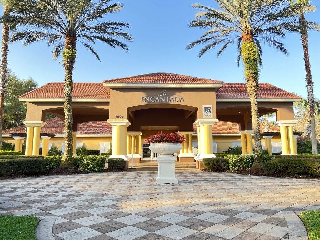 A hotel entrance with a checkered pavement, palm trees, and a large planter with flowers.