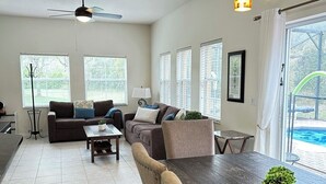 A spacious living room with a dark wooden coffee table, two sofas, and a ceiling fan. - Great home & location-private pool, forest view-near DISNEY & so much more! (Kissimmee)