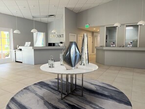 A modern reception area with a reception desk, a round table with metallic sculptures, and a large mirror.