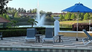 A pool area with lounge chairs, a fountain, and a view of a lake and buildings in the background. - Great home & location-private pool, forest view-near DISNEY & so much more! (Kissimmee)