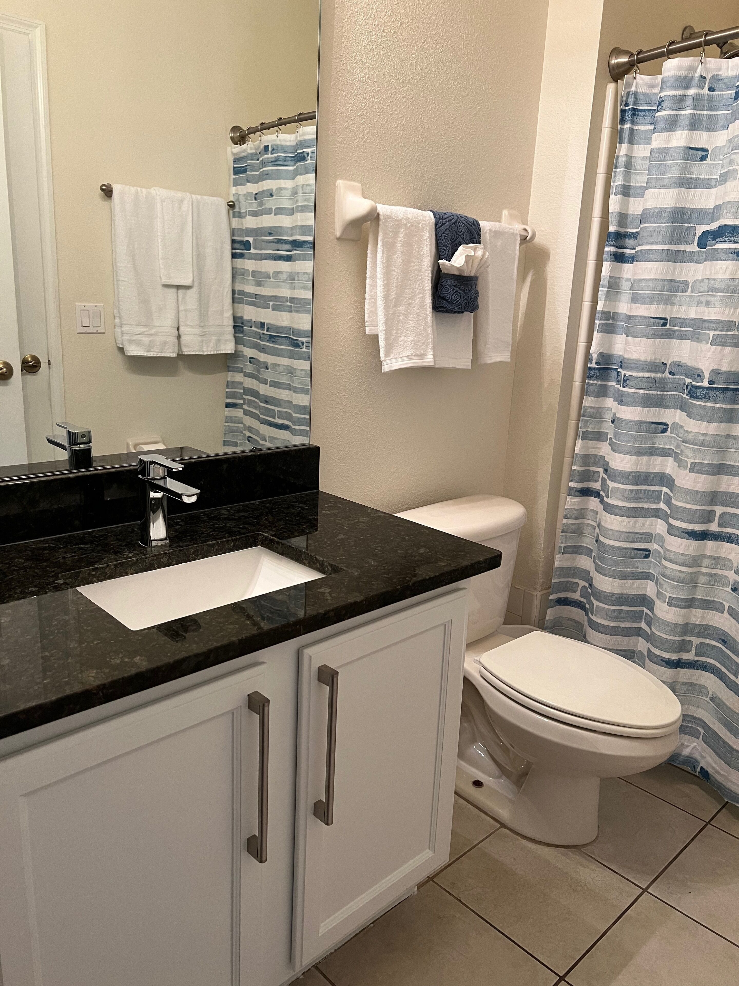 A bathroom with a black countertop sink, white cabinets, a white toilet, and a striped shower curtain.
