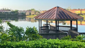 A gazebo with a metal roof over a dock, surrounded by lush greenery and a calm lake. - Great home & location-private pool, forest view-near DISNEY & so much more! (Kissimmee)