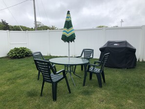 A backyard with a round table and four chairs, a green and yellow striped umbrella, and a Weber grill.