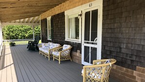 Eine überdachte Veranda mit Korbmöbeln, einem Grill und Blick auf einen bewaldeten Bereich.