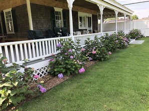 A covered porch with outdoor seating and a well-maintained garden with hydrangeas. - CHARMING HISTORIC ISLAND HOME--WEEKLY RENTAL-- OAK BLUFFS (Oak Bluffs)