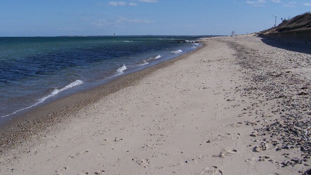 Ein Strand mit blauem Himmel, ruhigem Meer und sandigem Ufer.