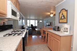 A kitchen with a stove, microwave, and coffee maker. There is a dining area with a table and chairs.
