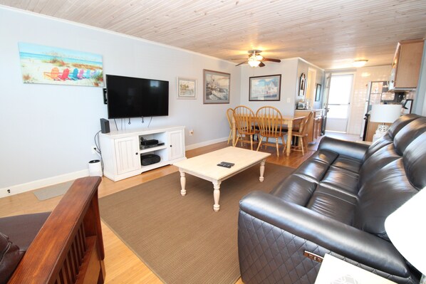 A living room with a television, a sofa, a coffee table, and a dining area with chairs and a table.