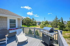 A deck with a grill, lounge chairs, and a window with flowers. - Cozy Duplex Retreat Close to Beaches! (1814) (West Dennis)