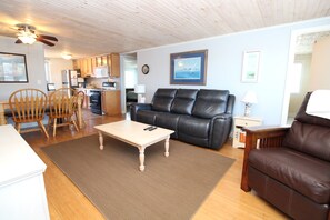 A living room with a sofa, chairs, a coffee table, and a kitchen in the background.