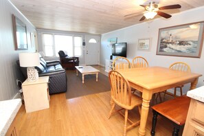 A living room with a sofa, a dining table with chairs, a television, and artwork on the walls. - Cozy Duplex Retreat Close to Beaches! (1814) (West Dennis)