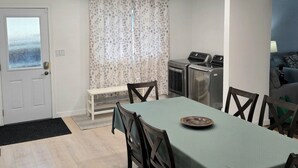 Uma sala de jantar com mesa, cadeiras e um banco. Há uma máquina de lavar no fundo.
