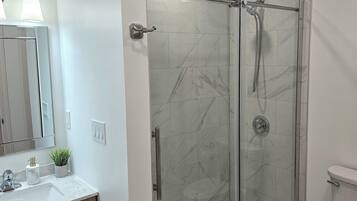 Une salle de bain moderne avec une douche à parois de verre, des toilettes blanches et un meuble-lavabo recouvert de carreaux de marbre.