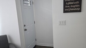Um corredor com uma porta branca, uma poltrona cinza e um tapete com padrão preto e branco.