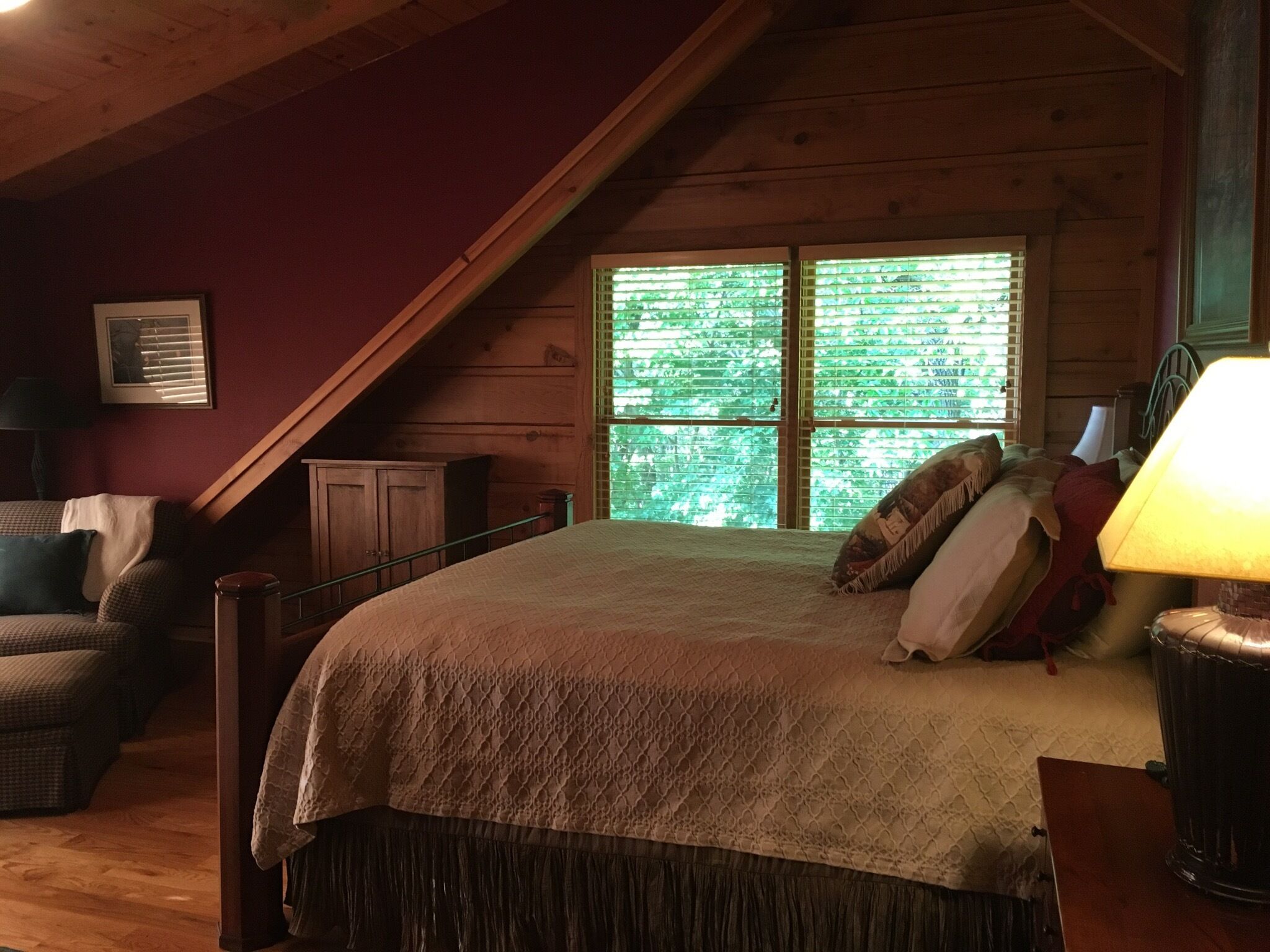 A cozy bedroom with a large bed, a wooden ceiling, and a window with blinds.