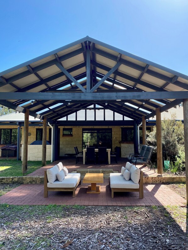 A covered patio area with a table and two sofas, a grill, and a dining table with chairs.