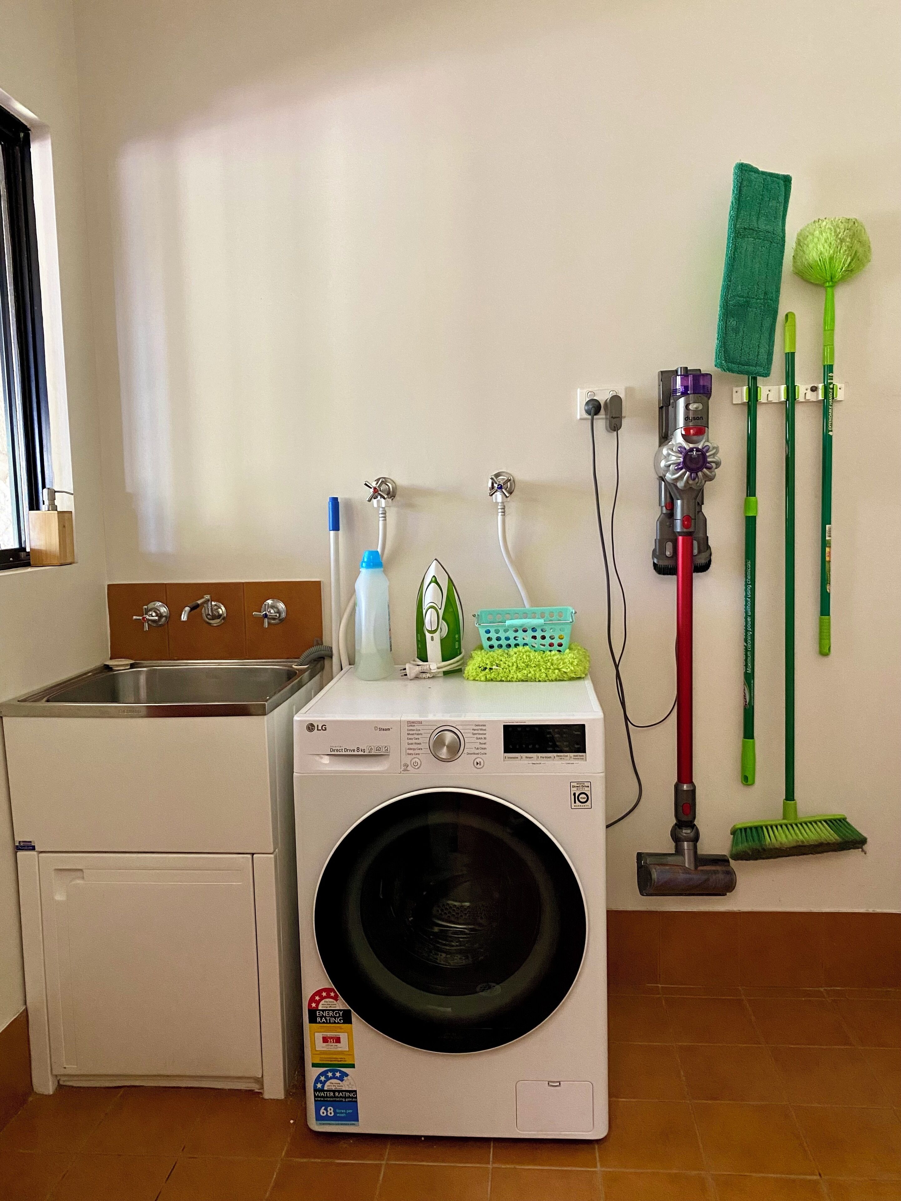 A laundry area with a washing machine, a sink, and various cleaning tools.