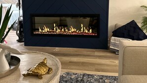 A modern living room with a dark blue accent wall, a flat-screen TV mounted above a fireplace, and a comfortable seating area with a patterned rug. - Direct Siesta Key Beachfront condo! (Siesta Key)