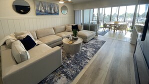 A modern living room with a sectional sofa, a round coffee table, and a large window offering a city view. - Direct Siesta Key Beachfront condo! (Siesta Key)