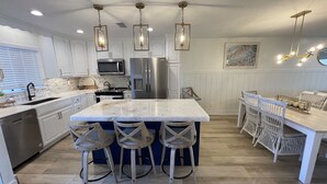 A modern kitchen with white cabinetry, a large island with bar stools, stainless steel appliances, and pendant lighting. - Direct Siesta Key Beachfront condo! (Siesta Key)