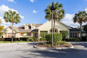 A residential building with a light yellow exterior, a central entrance with a covered porch, and a landscaped driveway. - Newly Renovated, Modern Two Bedroom Condo Minutes Away From Disney (Kissimmee)